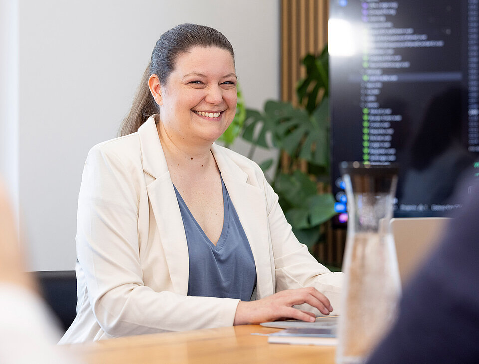 Carina Maucher von Rollout Solutions sitzt lächelnd an einem Tisch und arbeitet am Laptop