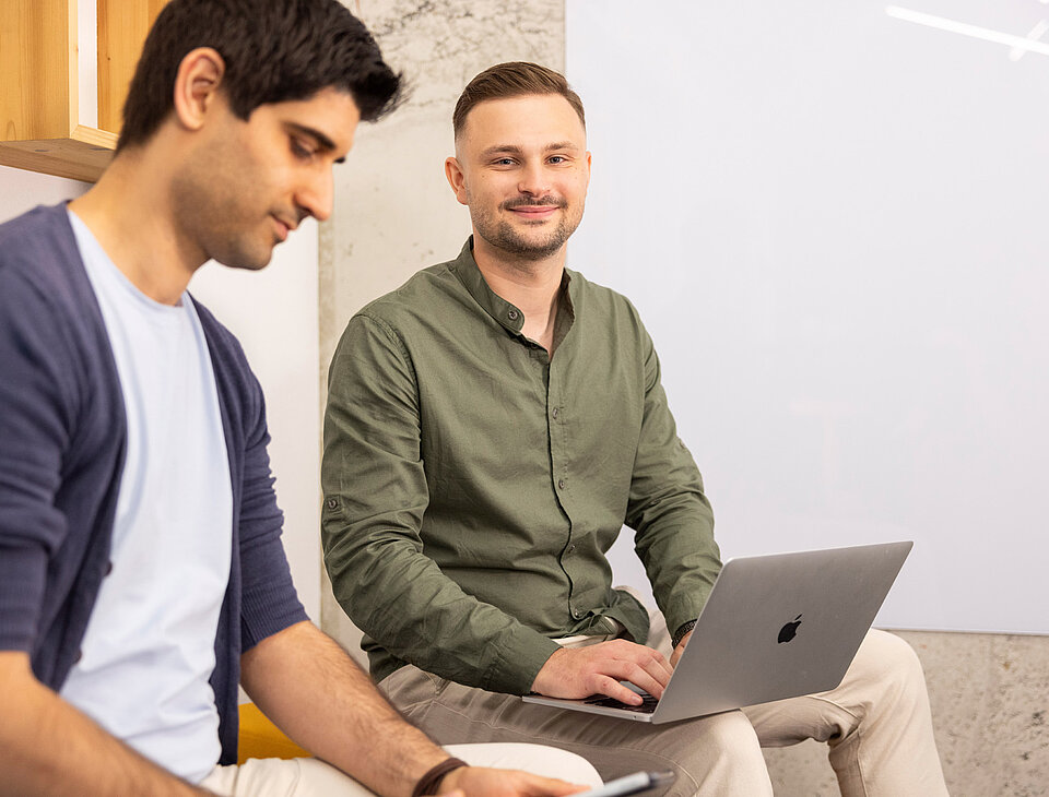 Tomislav Tomic und ein weiterer Mitarbeiter von Rollout Solutions sitzen nebeneinander und arbeiten am Laptop