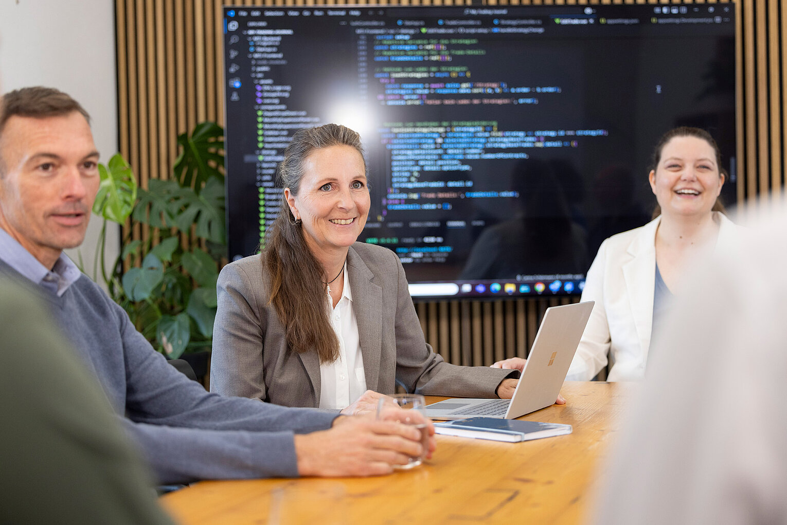 Alexandra Kreis von Rollout Solutions im Gespräch mit männlichen und weiblichen Kollegen, im Hintergrund ein Bildschirm
