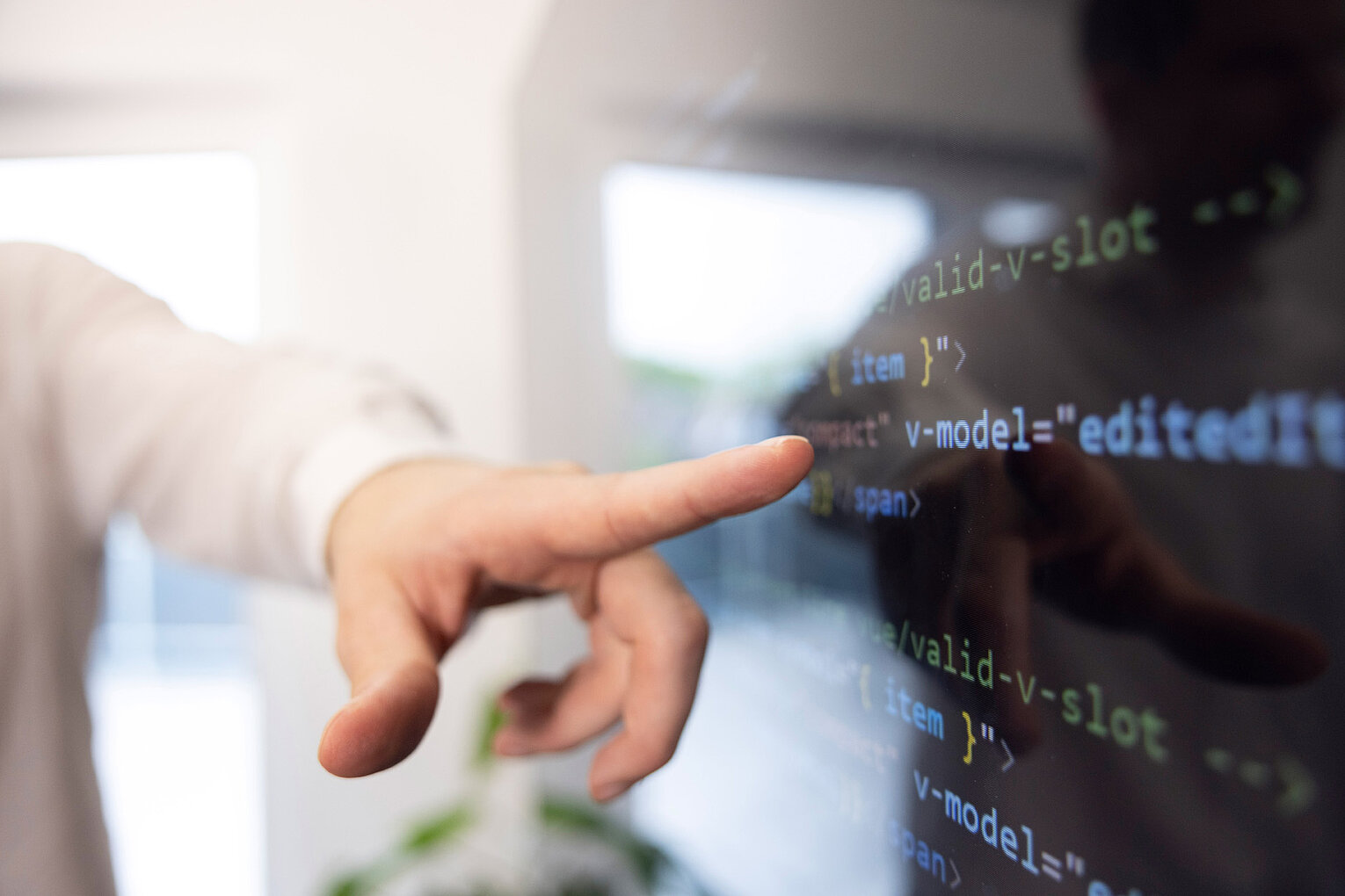 Ein Mann zeigt mit dem Zeigerfinger auf eine Codezeile auf einem großen Bildschirm