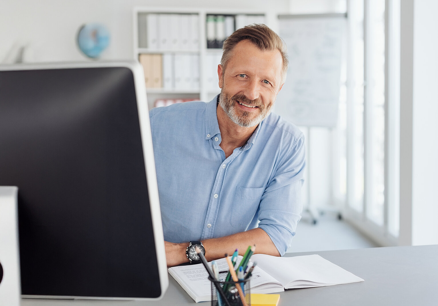 Mann mit Hemd sitzt am Laptop und schaut in die Kamera